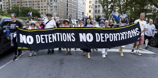 An der Spitze eines Demonstrationszuges, der durch die Straßen zieht, tragen mehrere Menschen ein Banner vor sich her, auf dem steht: "No Detentions! No Deportations!".