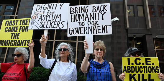 Das Foto zeigt vier Frauen bei einer Protestaktion vor einem Gebäude. Sie halten Schilder hochm auf denen unter anderem steht: "Dignity for Asylum Seekers". Oder: "First they came for the immigrants".