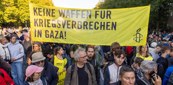 Das Foto zeigt mehrere Personen in einer riesigen Menschenmenge, die ein Banner hochhalten mit Amnesty-Logo und dem Schriftzug "Keine Waffen für Kriegsverbrechen in Gaza!"