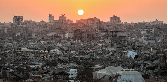 Das Foto zeigt einen Sonnenuntergang über einer fast komplett zerstörten Stadt.