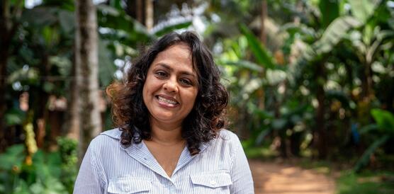 Das Foto zeigt Ashila Dandeniya, die lächelnd auf einem Weg zwischen Palmen, Bäumen und Sträuchern steht.