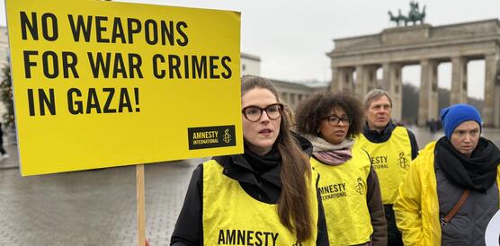 Mehrere Menschen mit gelben Leibchen mit der Aufschrift "Amnesty" und Protestplakaten