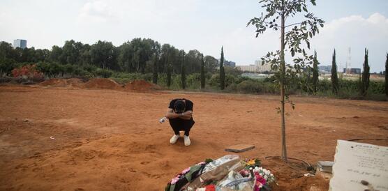 Das Foto zeigt einen jungen Mann, der neben einem Grab kauert. Neben dem Grab steht ein Baum.