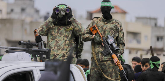 Das Foto zeigt zwei uniformiere und maskierte Männer. Der Mann links blickt durch ein Fernglas. Der Mann rechts hält ein Scharfschützengewehr in den Händen.
