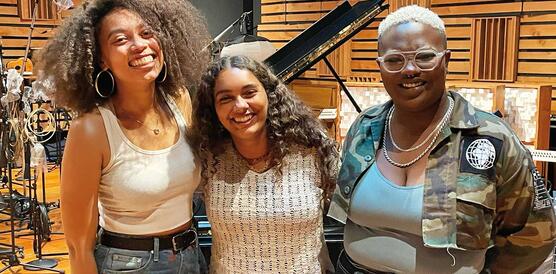 Drei Mitglieder der kalifornischen Band "Oakland Rising" stehen in einem Konzertsaal vor einem Flügel und Mikrofonständern.