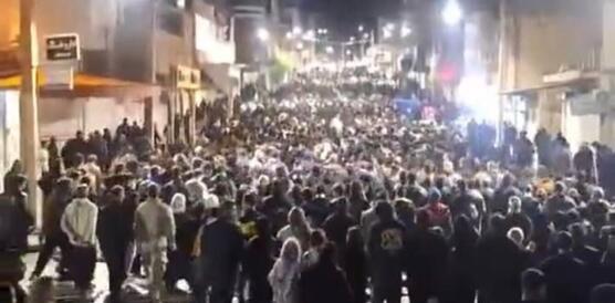 Das Foto zeigt einen großen Demonstrationszug, der nachts durch die beleuchtete Straße in einer Stadt zieht.