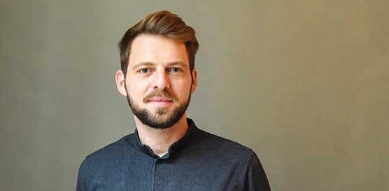 Ein jnuger Mann mit kurzen Haaren und Bart, er trägt ein Hemd.