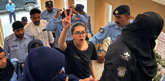 Eine Frau ist umringt von Polizeibeamten und -beamtinnen. Sie hebt die rechte Hand und macht das Victory-Zeichen