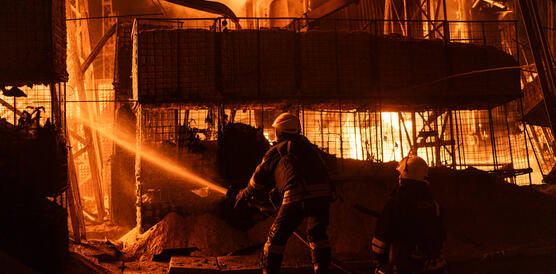 Das Foto zeigt einen Feuerwehrmann mit Wasserschlauch vor einem Gebäude, das lichterloh in Flammen steht.