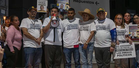 Eine Gruppe von Menschen bei einer Kundgebung, eine Person hält ein Megafon, sie tragen weiße T-Shirts mit der Aufschrift: "Befreit alle politischen Gefangenen"