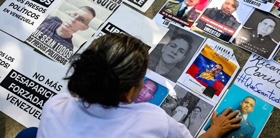 Eine Person bückt sich über zahlreiche Porträts und Dokumente, die am Boden liegen. Sie zeigen politische Gefangene in Venezuela.