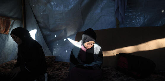 Zwei Frauen mit Kopftüchern sitzen traurig und niedergeschlagen im Halbdunkel in einem Zelt. Sie blicken auf den Boden. Auf das Gesicht der Frau rechts fällt ein Lichtstrahl