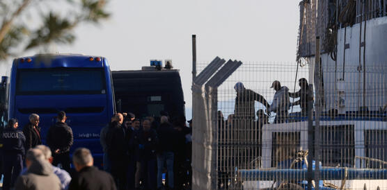 Polizeifahrzeuge stehen an einer Grenze, zu sehen sind Personen, die von Beamten abgeführt werden