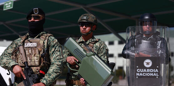 Drei schwer ausgerüstete Mitglieder der mexikanischen Armee und Nationalgarde stehen mit Waffen, taktischem Gerät und einem Schutzschild bei einer Übung nebeneinander.
