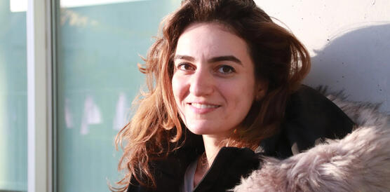 Eine junge Frau mit offenem Haar lächelt, sie trägt eine Art Pelz um die Schultern.