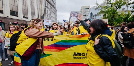 Das Foto zeigt mehrere Personen mit Amnesty-Leibchen an der Spitze eines Demonstrationszuges. Viele Lachen, andere tragen Mundschutz. Sie halten ein Banner vor sich mit Regenbogenfarben und dem Amnesty-Logo.