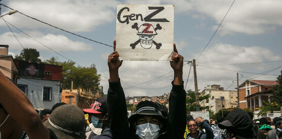 Eine Person mit Mundschutz hält bei einer Demonstration ein Plakat hoch, auf dem ein Totenschädel mit Knochen abgebildet ist. Darüber steht: "Gen Z".