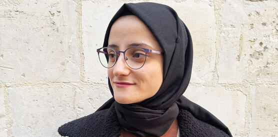 Eine junge türkische Frau mit Kopftuch, Brille, Lederjacke, Wollpulli.