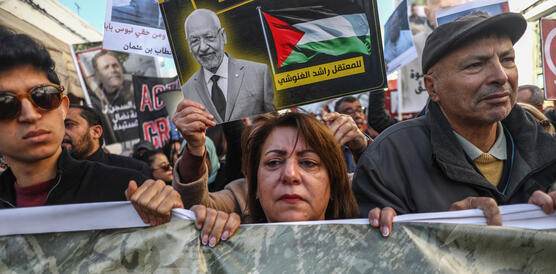 Das Foto zeigt einen jüngeren Mann, eine Frau und einen Mann, die bei einer Demonstration ein Banner vor sich hertragen. Hinter ihnen hält eine Person ein Plakt hoch mit dem Fotos Mannes.