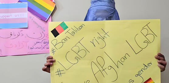 Eine Person trägt Niqab und hält ein Schild mit handgeschriebenen Hashtags: #BanTaliban, #LGBTright, #SaveAfghanLGBT, #Transgender.