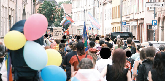 Eine Menschenmenge in einer Straße, rechts und links Altbau-Häuserfronten, Menschen demonstrieren, manche haben Luftballons dabei.