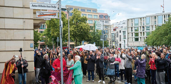 Menschen an einer Straßenecke in Berlin versammeln sich zur Enthüllung eines neuen Straßenschilds.