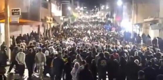 Das Foto zeigt einen großen Demonstrationszug, der nachts durch die beleuchtete Straße in einer Stadt zieht.