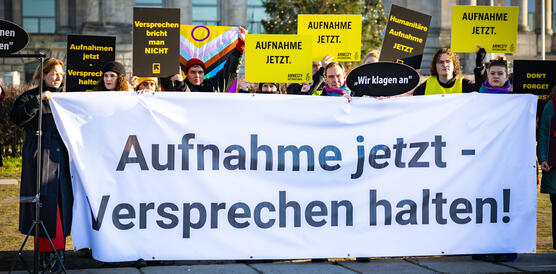 Mehrere Personen protestieren mit Schildern und Papptafeln. Sie halten ein Banner vor sich, auf dem steht: "Aufnahme jetzt – Versprechen halten!"