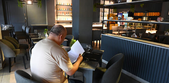 Ein mittelalter Mann sitzt in einem Hotelrestaurant an einem Tisch und liest ein Dokument.