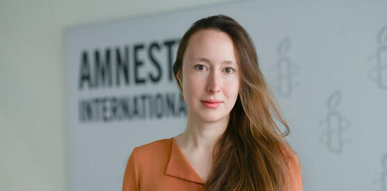 Porträtfoto von Elisabeth Oberthür. Auf der Wand im Hintergrund ist eine große Tafel angebracht mit dem Schriftzug "Amnesty International".