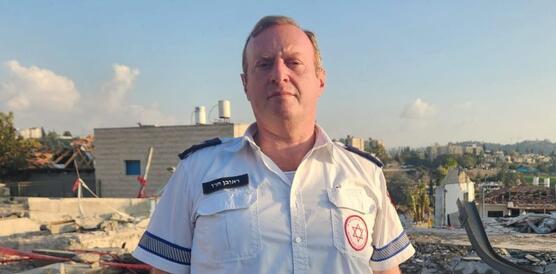 Das Foto zeigt Reuven Harow in seiner Uniform vor den Trümmern eines Gebäudes stehen unter blauem Himmel. Er blickt ernst in die Kamera.