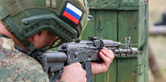 Das Foto zeigt einen von hinten fotografierten Soldaten, der sein Sturmgewehr angelegt habt zum Zielen. Er trägt einen Helm, auf dem eine kleine russische Flagge platziert ist.