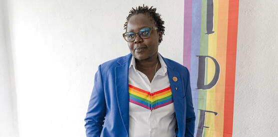 Eine Person im Anzug, darunter ein Hemd mit einem Keil in Regenbogenfarben, die Haare in kurzen Dreadlocks, eine Hornbrille aug, es ist die Pastorin Caroline Omolo