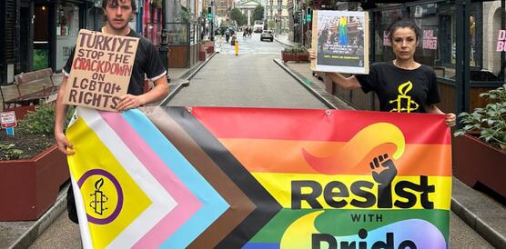 Das Foto zeigt einen jungen Mann und eine junge Frau in einer schmalen Straße. Sie tragen Amnesty-T-Shirts und halten die Intersex-Inclusive-Pride-Flagge vor sich, auf dem steht "Resist with pride". Sie halten außerdem kleine Plakate in der Hand. Auf dem des Mannes steht: "Turkiye, stop the crackdown on LGTBIQ+ rights".