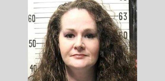 Polizeiaufnahme (Mugshot) von Christa Pike. Frontale Porträtaufnahme vor einer Wand mit genauer Größentabelle im Hintergrund.