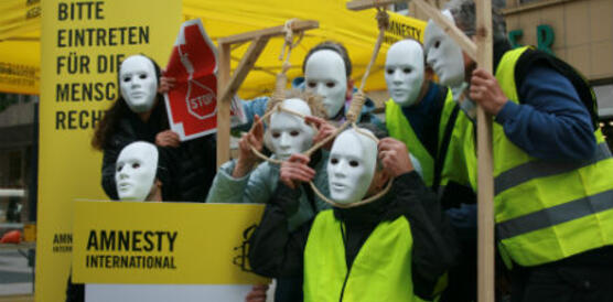 Menschen mit weißen Masken imitieren die Todesstrafe mit Galgen
