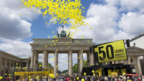 Menschenmenge feiert vor Brandenenburger Tor mit Luftballons, Bus und Schildern