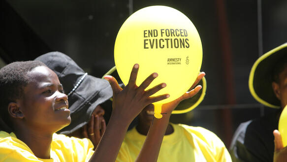 Junger Mensch hält Luftballon mit der Aufforderung "End forced evictions" in die Höhe