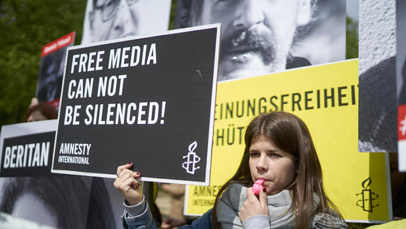 Junge Frau mit Trillerpfeife vor Protestplakaten zum Thema Meinungsfreiheit