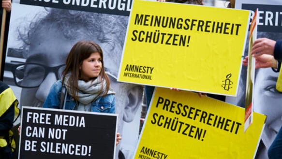 Junge Frau steht vor Plakaten zum Thema Meinungsfreiheit