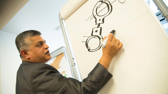 Mann zeichnet mit Filzstift Handschellen auf eine Flip-Chart-Tafel