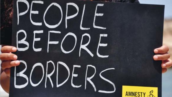 Ein Schild mit der Aufschrift "People before borders" wird groß in den Bildausschnitt gehalten.
