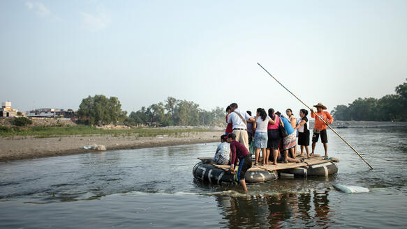 Eine Gruppe von Menschen versucht mit einem Floß einen Fluss zu überqueren