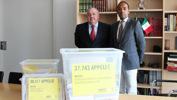 Zwei Männer im Anzug vor zwei großen Kisten mit Petitionen