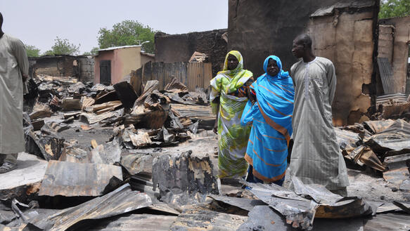 Drei Menschen stehen mitten in verbrannten Überresten mehrerer Häuser und Geschäfte
