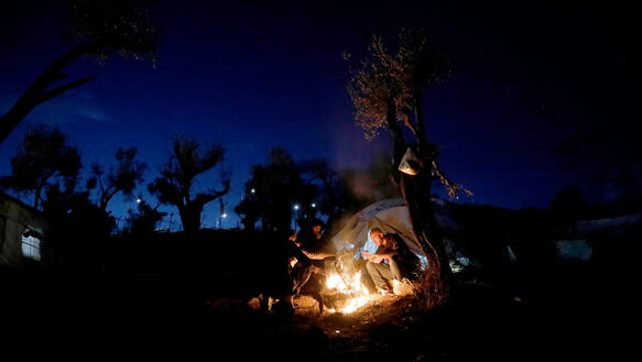 Drei Männer sitzen im Dunkeln draußen um ein Lagerfeuer