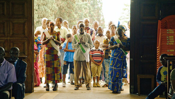 Filmszene aus "Das Kongo Tribunal": Eine Gruppe von Erwachsenen und Kindern stehen vor einer großen Tür und blicken ins Innere