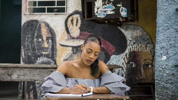 Eine junge Frau sitzt mit Stift und Block an einem Tisch und schreibt