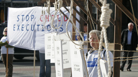 Mehrere Galgenstricke, im Hintergrund ein großes Banner mit der Aufschrift "Stop Child Executions"