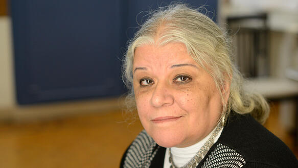 Eine ältere Frau mit längeren, grauen Haaren in einem Büro schaut freundlich in die Kamera